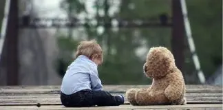 Young boy sitting beside teddy bear