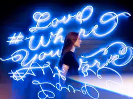 lady in front of neon blue lights that read love where you are