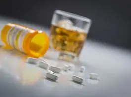 glass of alchohol and open bottle of pills