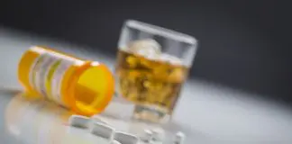 glass of alchohol and open bottle of pills