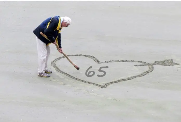 HRHQ Retire 65 retired man writing 65 in sand on beach
