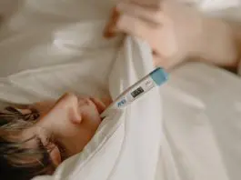 man under duvet with thermometer in mouth
