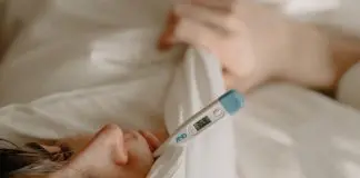 man under duvet with thermometer in mouth