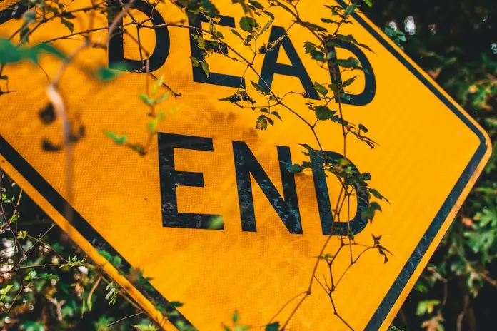 yellow "dead end" sign overgrown with bush