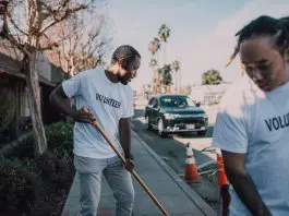 two men sweeping outside with "volunteer" t-shirts on