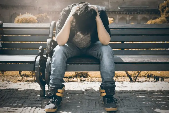 man sitting on bench with his head in his hands