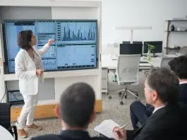 lady presenting at a monitor full of graphs and charts to small audience