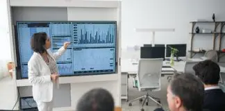 lady presenting at a monitor full of graphs and charts to small audience