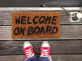 welcome mat with words "welcome on board" with red sneakers of person standing on it visible