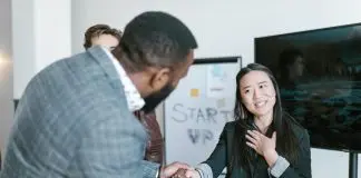 man shaking womans hand thanking her with colleague looking on