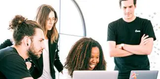 A Group of smiling Professionals huddled around laptops Sharing Ideas