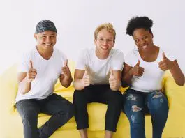 3 people sitting on yellow sofa with big smiles giving a thumbs up