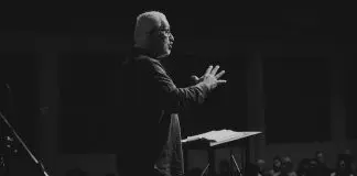 black and white phot of man with beard speaking to a crowd from a stage