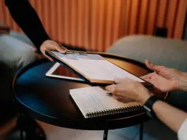person handing cv, attached to a clipboard, accross desk