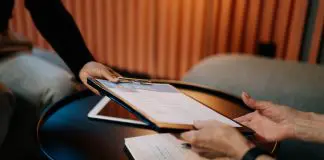 person handing cv, attached to a clipboard, accross desk