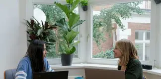 two women sitting at a conference table with laptops chatting