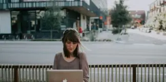lady sitting at a table on sidewalk working on apple laptop