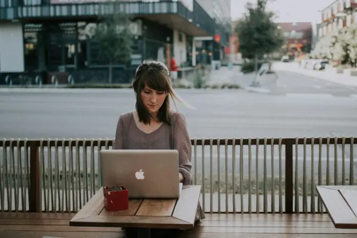 christin-hume-slbqShqAhEo-unsplash lady sitting at a table on sidewalk working on apple laptop