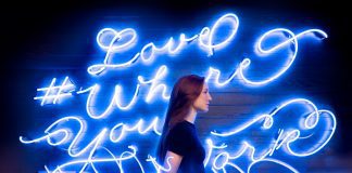 lady in front of neon blue lights that read love where you are