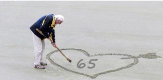 retired man writing 65 in sand on beach