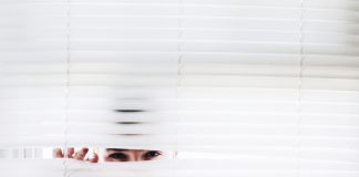 man peeking through venetian blind