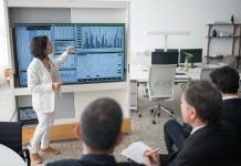 lady presenting at a monitor full of graphs and charts to small audience