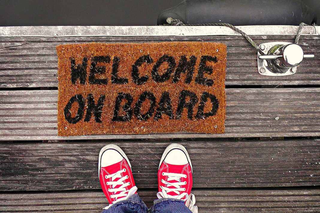 welcome mat with words "welcome on board" with red sneakers of person standing on it visible