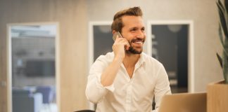 smiling man on mobile phone sitting at laptop with coffee