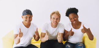 3 people sitting on yellow sofa with big smiles giving a thumbs up